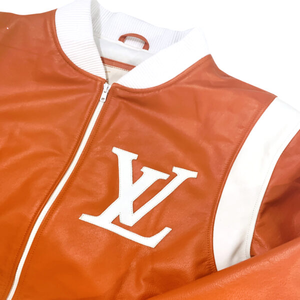 Close-up of Louis Vuitton orange bomber jacket with white accents on shoulders, white cuffs, collar and hem. White LV logo on left front chest 