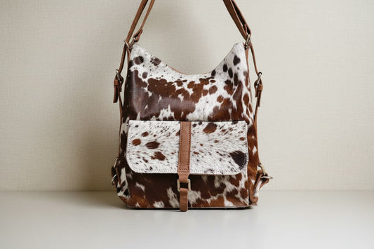 Brown and white cow print backpack shoulder bag with leather straps on a light background