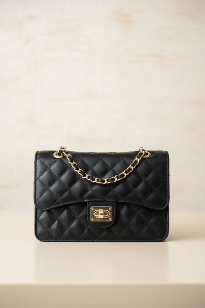Black quilted handbag with gold chain and clasp on a beige background