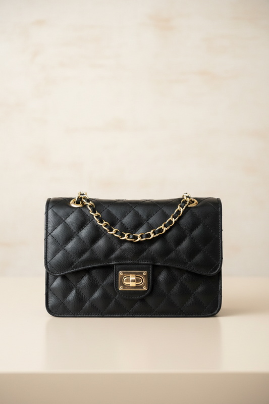 Black quilted handbag with gold chain and clasp on a beige background