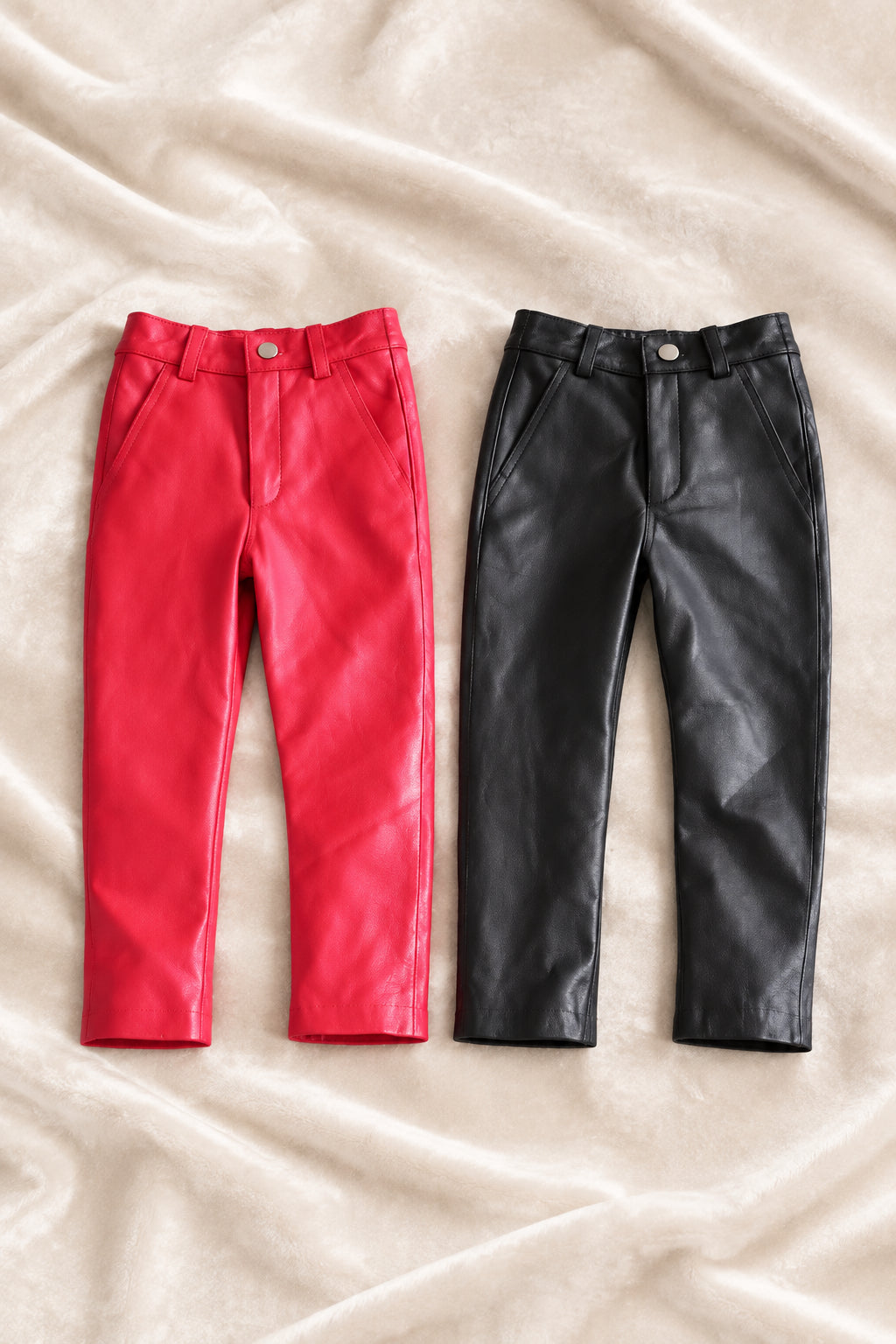 kids black leather pants and red leather pants laid over a velour fabric front view