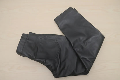 Black leather pants folded on a light wood surface, showing the back pocket and waistband details.