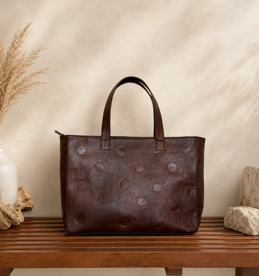 Front view of oxblood debossed leather tote bag with double handles kept on a wooden bench 