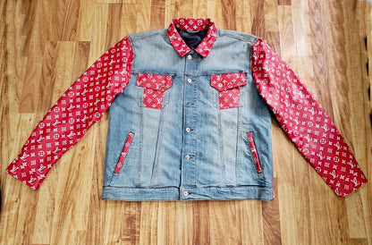 trucker Denim jacket with white designer monogram pattern on red leather sleeves and pockets laying flat on a wooden surface