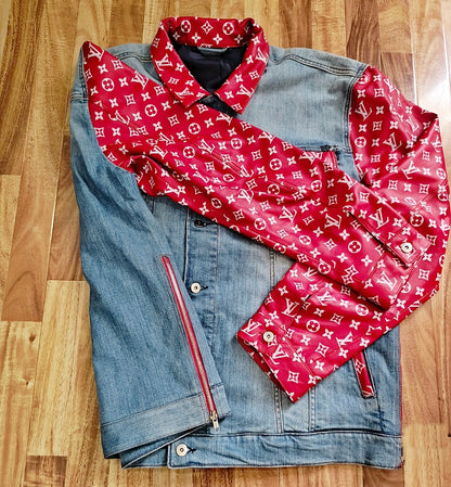 trucker Denim jacket with white designer monogram pattern on red leather sleeves and pockets laying flat on a wooden surface