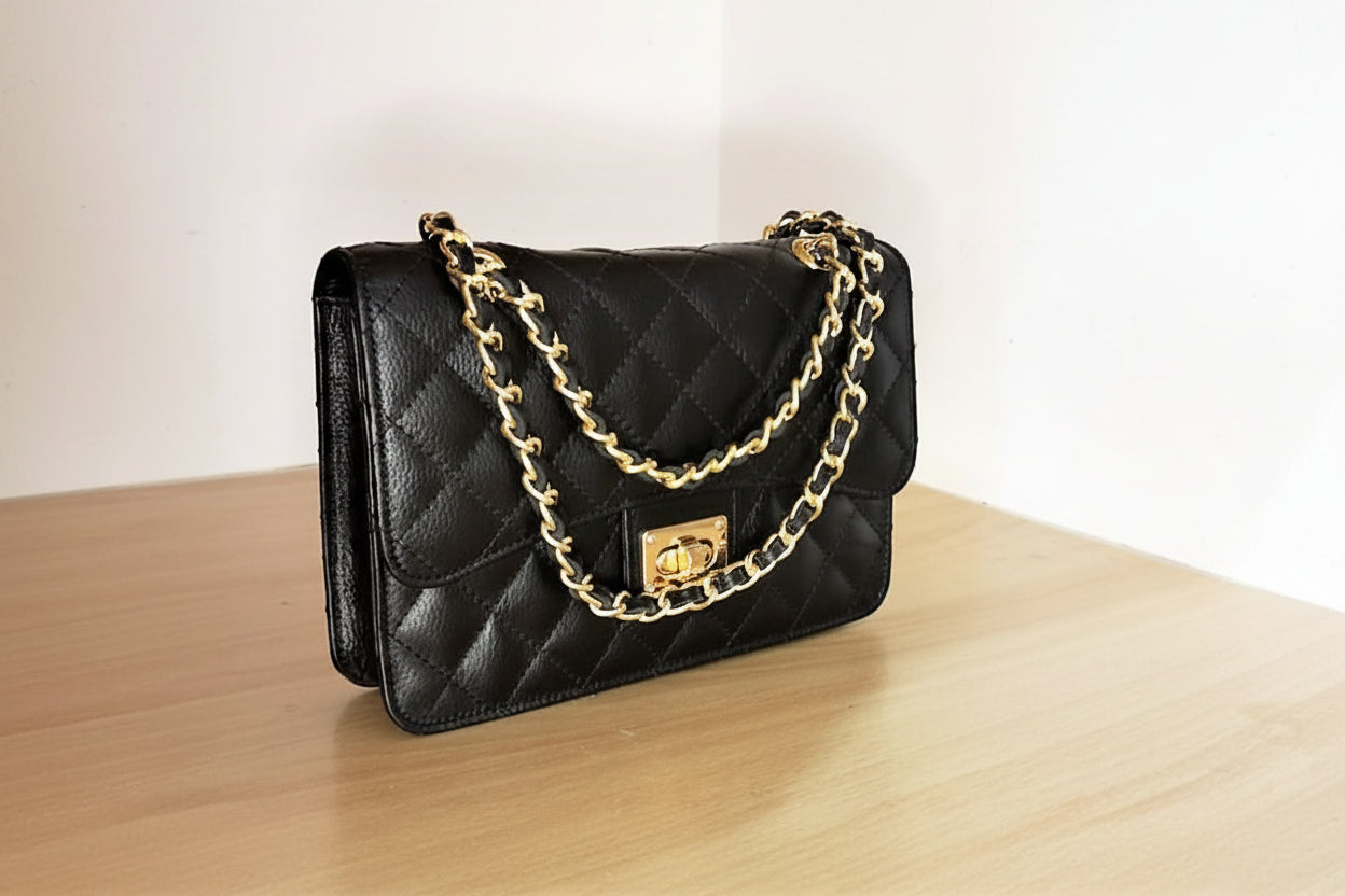 a black premium leather quilted leather puse on a beige wooden surface a white wall behind